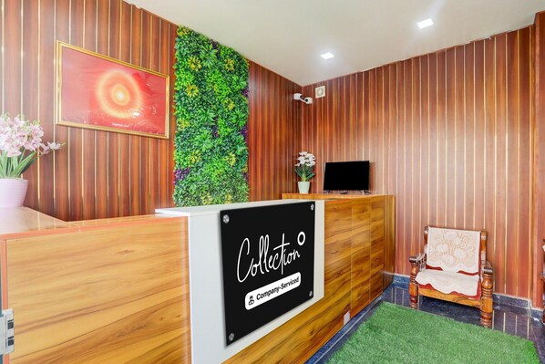 A reception desk with a sign reading 'Collection Company Serviced,' a television, a potted plant, and a decorative chair.