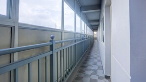 A corridor with a metal railing, large windows, and a tiled floor.