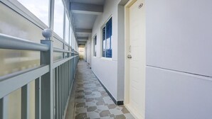 A corridor with a tiled floor, a metal railing, and a door with a number sign.