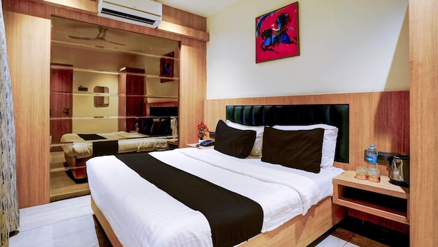 A hotel room with a large bed, a wardrobe, a mirror, a painting on the wall, and an air conditioning unit. - Townhouse Oak New Nashik Highway (Bhiwandi)