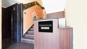Un comptoir d’accueil portant l’inscription « TOWNHOUSE », agrémenté d’un panneau indiquant qu’il s’agit d’un service de l’entreprise, un escalier avec un mur rose et un sol en marbre noir.