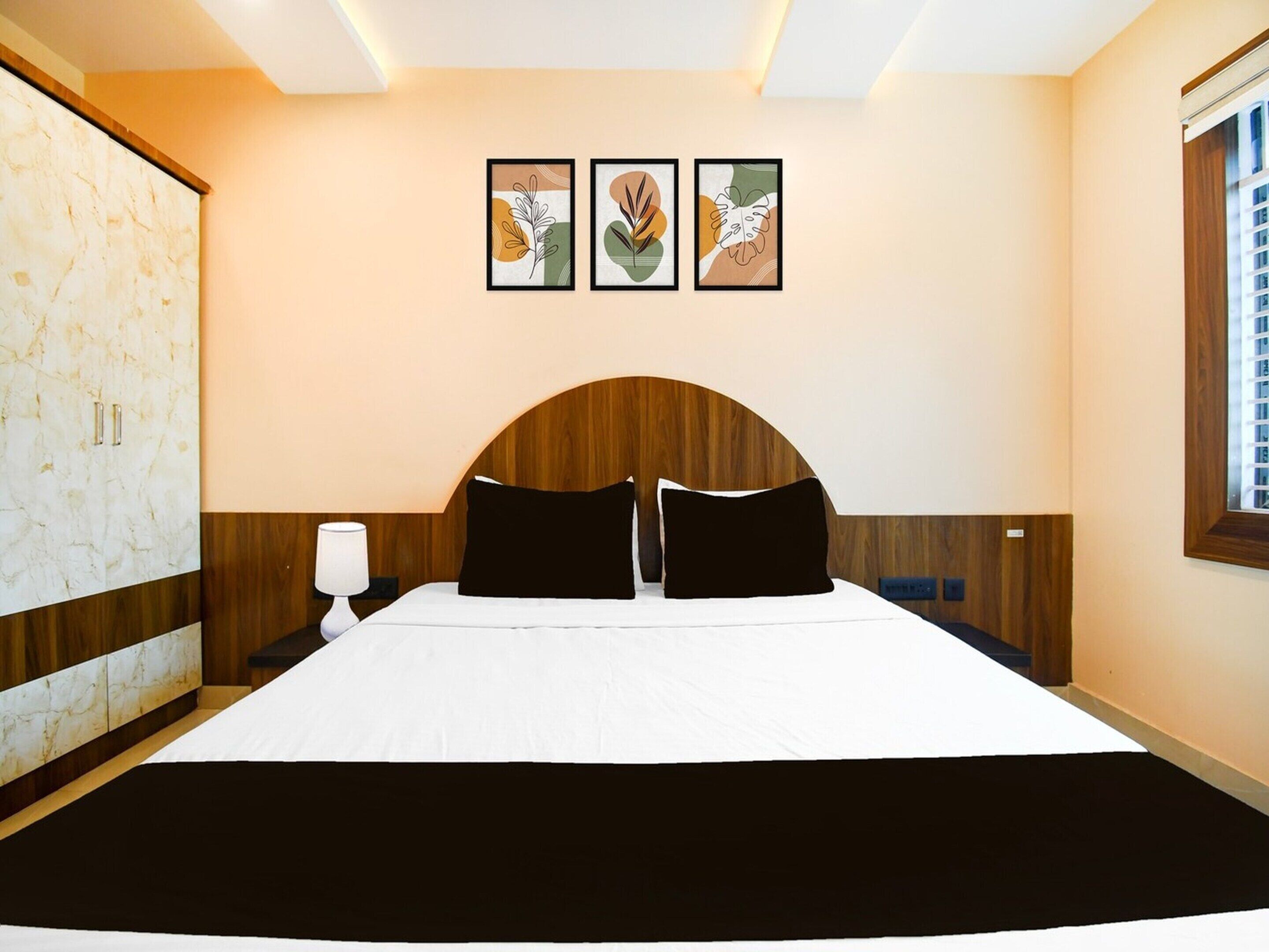 A hotel room with a bed, a wardrobe, and three framed artworks on the wall.