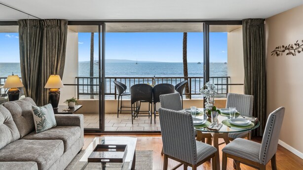 Un salón moderno con balcón con vistas al mar, amueblado con un sofá, sillas y una mesa de comedor.