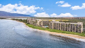 Un hotel costero con varias edificaciones, una playa y montañas al fondo.