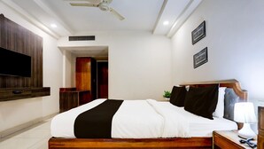 Quarto com cama, mesa de cabeceira, abajur e televisão na parede.