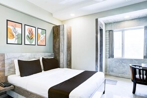 A hotel room with a bed, a desk, a chair, and framed artwork on the wall.