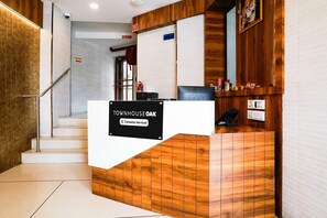 A reception desk with a sign indicating it is serviced by a company, a fire hose rest sign, and an elevator sign. - Super Townhouse Oak Vashi (Navi Mumbai)