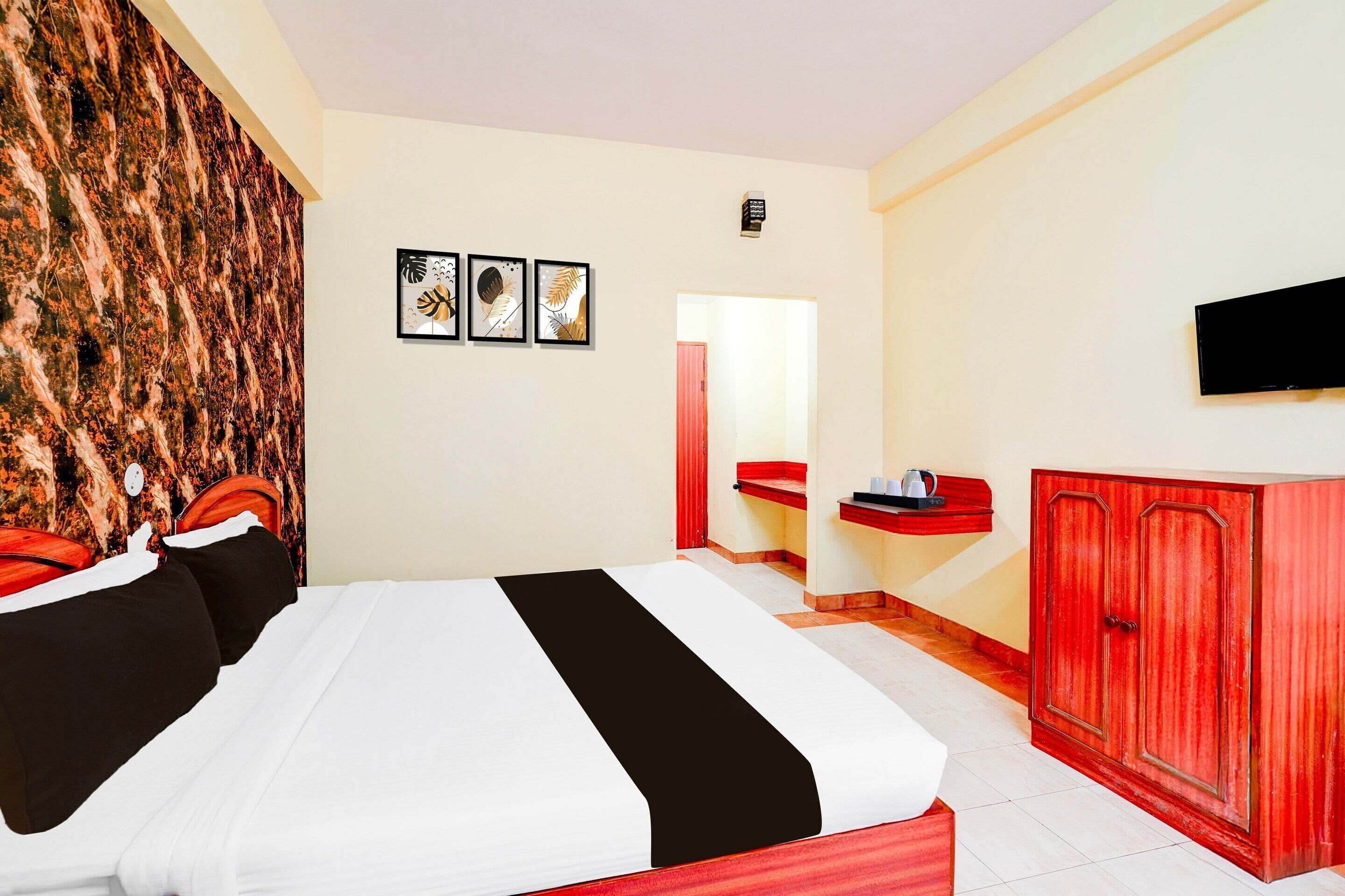 A hotel room with a bed, a red wardrobe, a TV mounted on the wall, and a bathroom visible through an open door.