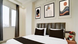 Ein Hotelzimmer mit einem großen Bett, einem Nachttisch mit Blumenvase und drei gerahmten Kunstwerken an der Wand.