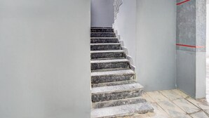 A staircase with stone steps leading to a landing, a grey wall, and a window with a view. - Premium oyo Nagaram (Hyderabad)