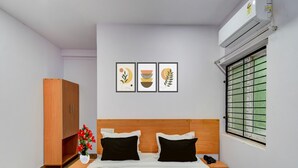 A bedroom with a wooden headboard, a bed with black and white bedding, a nightstand with a phone, a wooden wardrobe, and three framed wall art pieces. - Premium oyo Nagaram (Hyderabad)