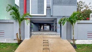 A building entrance with a concrete pathway, palm trees, and a grey facade. - Premium oyo Nagaram (Hyderabad)