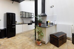 Eine Küche mit einem schwarzen Kühlschrank, einem Blumentopf, einer Holzkiste und einer weißen Küchenzeile.