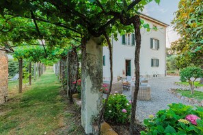 A white building with green shutters, a gravel courtyard, and a vine-covered pergola. - Villa Near Lucca With Tuscan Garden Views (Capannori)