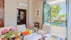 A dining area with a table set for six, a vase with flowers, and a view of the outdoors. - Villa Near Lucca With Tuscan Garden Views (Capannori)