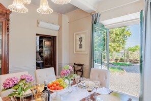 A dining area with a table set for six, a vase with flowers, and a view of the outdoors. - Villa Near Lucca With Tuscan Garden Views (Capannori)