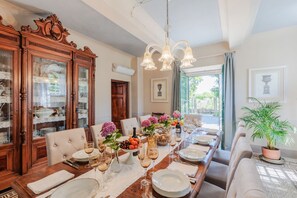 A dining room with a long wooden table set for a meal, flanked by tall cabinets with glass doors, a chandelier, and a view of the outdoors. - Villa Near Lucca With Tuscan Garden Views (Capannori)