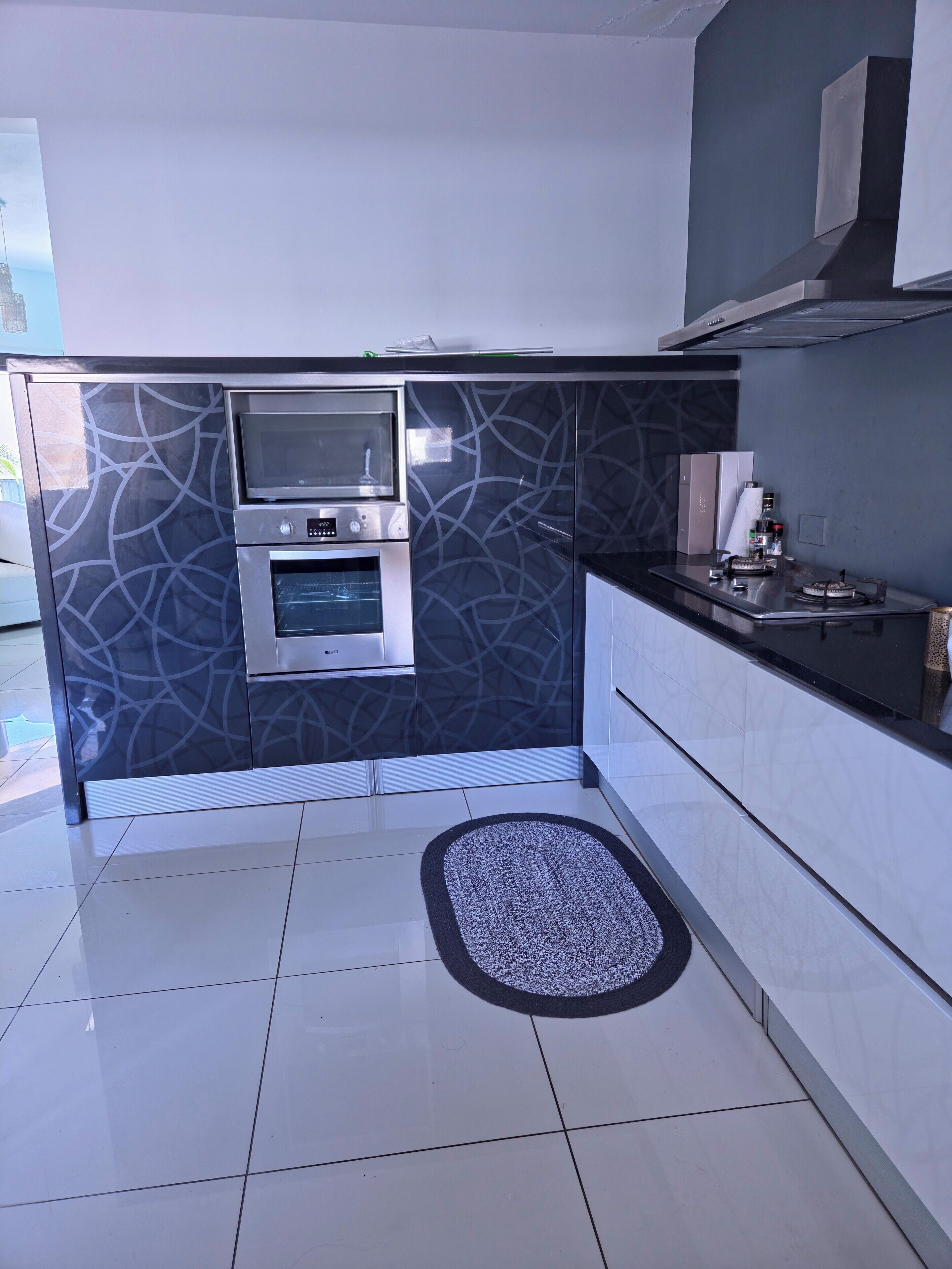 A modern kitchen with a built-in oven, microwave, and a small countertop with a kettle and a bottle.
