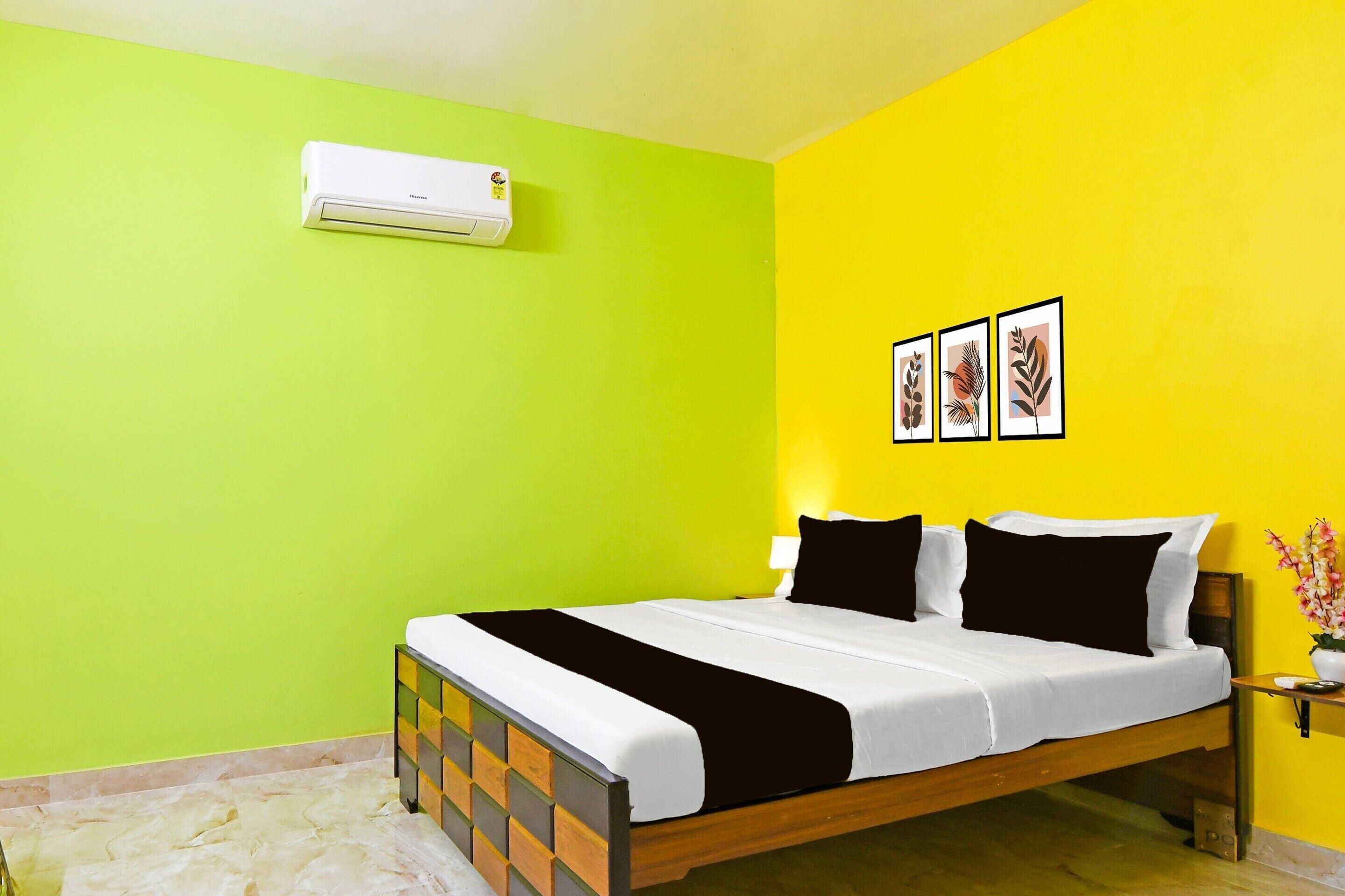 A hotel room with a bed, a nightstand, a wall-mounted air conditioner, and framed artwork on the wall.