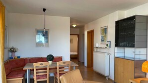 Un espace repas comprenant une table et des chaises, un canapé, un radiateur, ainsi qu’un coin cuisine avec des placards et un plan de travail.