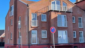 Un immeuble en briques à plusieurs étages, doté de balcons, d’un panneau indiquant qu’il est interdit de se garer et d’un lampadaire.