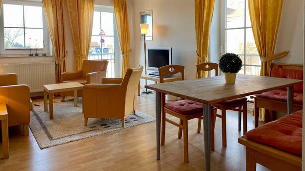 Une pièce avec une table à manger en bois, des chaises, un téléviseur et des rideaux jaunes.