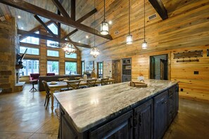 A spacious kitchen with a marble countertop, wooden beams, and pendant lighting. - Sleeps 21 • 4 King Ensuites • Game Room, Hot Tub & Outdoor Fun (Broken Bow)