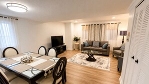 A living room with a sofa, TV, and a dining area with a table and chairs. - Stylish 3-bedroom Oakland apartment near universities, hospitals, and downtown. (Pittsburgh)