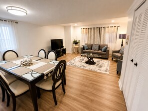 Ein Wohnzimmer mit Sofa, Fernseher und einer Essecke mit Tisch und Stühlen.