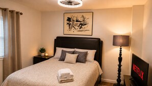 A neatly made bed with a patterned bedspread, a bedside lamp, a TV displaying 'NETFLIX,' and a framed artwork above the bed. - Stylish 3-bedroom Oakland apartment near universities, hospitals, and downtown. (Pittsburgh)