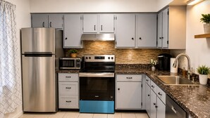 A modern kitchen with grey cabinets, stainless steel appliances, a granite countertop, and a blue dishwasher. - Stylish 3-bedroom Oakland apartment near universities, hospitals, and downtown. (Pittsburgh)