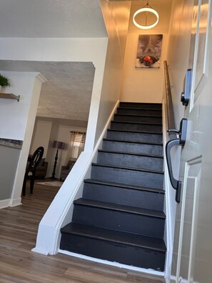 Eine Treppe mit Handlauf, eine Tür rechts und eine Wandleuchte.