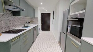 Una cocina estrecha con salpicadero de baldosas en espiga, una encimera con tabla de cortar y un refrigerador.