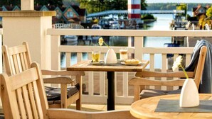 Eine Holzterrasse mit Tisch und Stühlen mit Blick auf einen Hafen voller Boote und einem Leuchtturm.