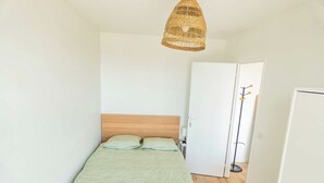 A bedroom with a wooden bed, a woven light fixture, a white wardrobe, and a door with a coat rack. - Private Room in a Shared Apartment - Bron (Bron)