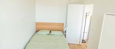 Makuuhuoneessa on puinen sänky, punottu valaisin, valkoinen vaatekaappi ja ovi, jossa on naulakko.