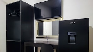 A modern room with a desk, a black wardrobe, a window with blinds, and a water dispenser.