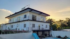 Un hotel de dos pisos con un balcón en el nivel superior, una zona de piscina y una escalera que conduce a la planta alta.