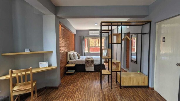Een kamer met een bed, een bureau, een stoel, een hanglamp en een deur.