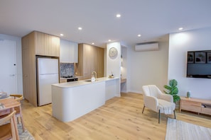 A modern kitchen with a central island, wooden cabinetry, and a built-in stove. - The Scandi: A Designer Dual Suite Retreat | Mt Ainslie Views (Dickson)