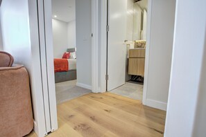 A hallway with a wooden floor leading to a bedroom with a bed and a red pillow. - The Scandi: A Designer Dual Suite Retreat | Mt Ainslie Views (Dickson)