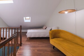 A bedroom with a wooden floor, a bed with checkered bedding, a yellow armchair, and a hanging light fixture. - 5-Bedroom House – View of the Cathedral – Vieux Mans – Sleeps 11 (Le Mans)