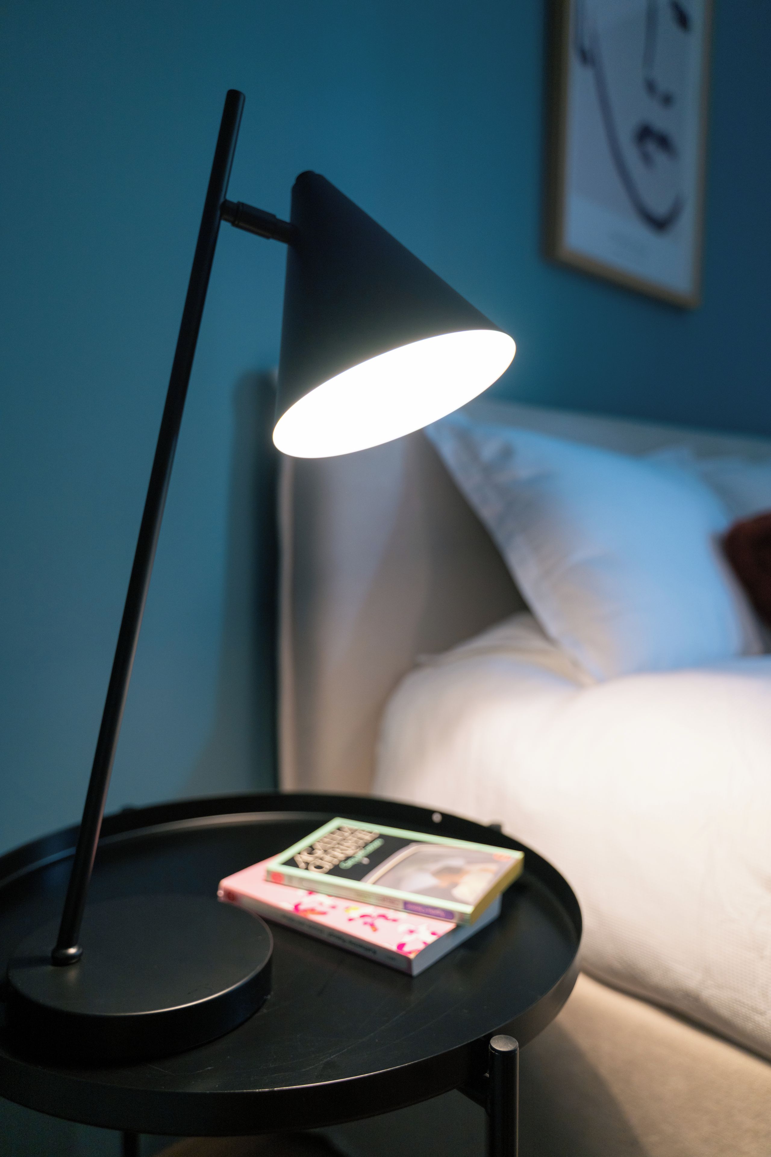 Ein Nachttisch mit Lampe, Buch und einem Bett mit weißer Bettwäsche.