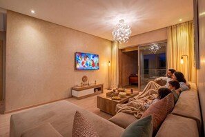 A living room with a sofa, TV, and a chandelier. - 3BR Prestigia | Pool | Parking | 12min Centre (Marrakesh)