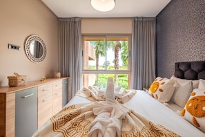A bedroom with a bed, a bedside table, a mirror, and a window with a view of palm trees. - 3BR Prestigia | Pool | Parking | 12min Centre (Marrakesh)