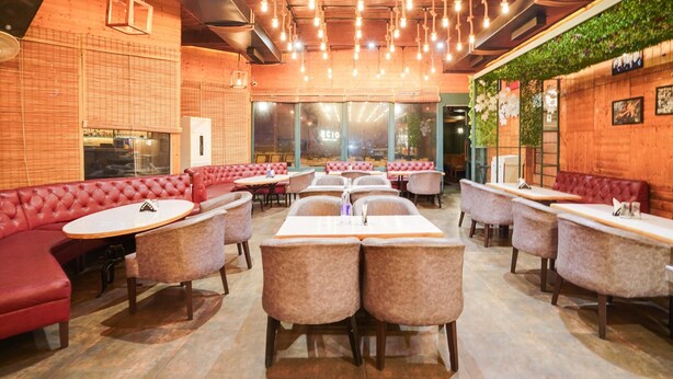 Un interior de restaurante con asientos tipo banca rojos, mesas redondas y lámparas colgantes.