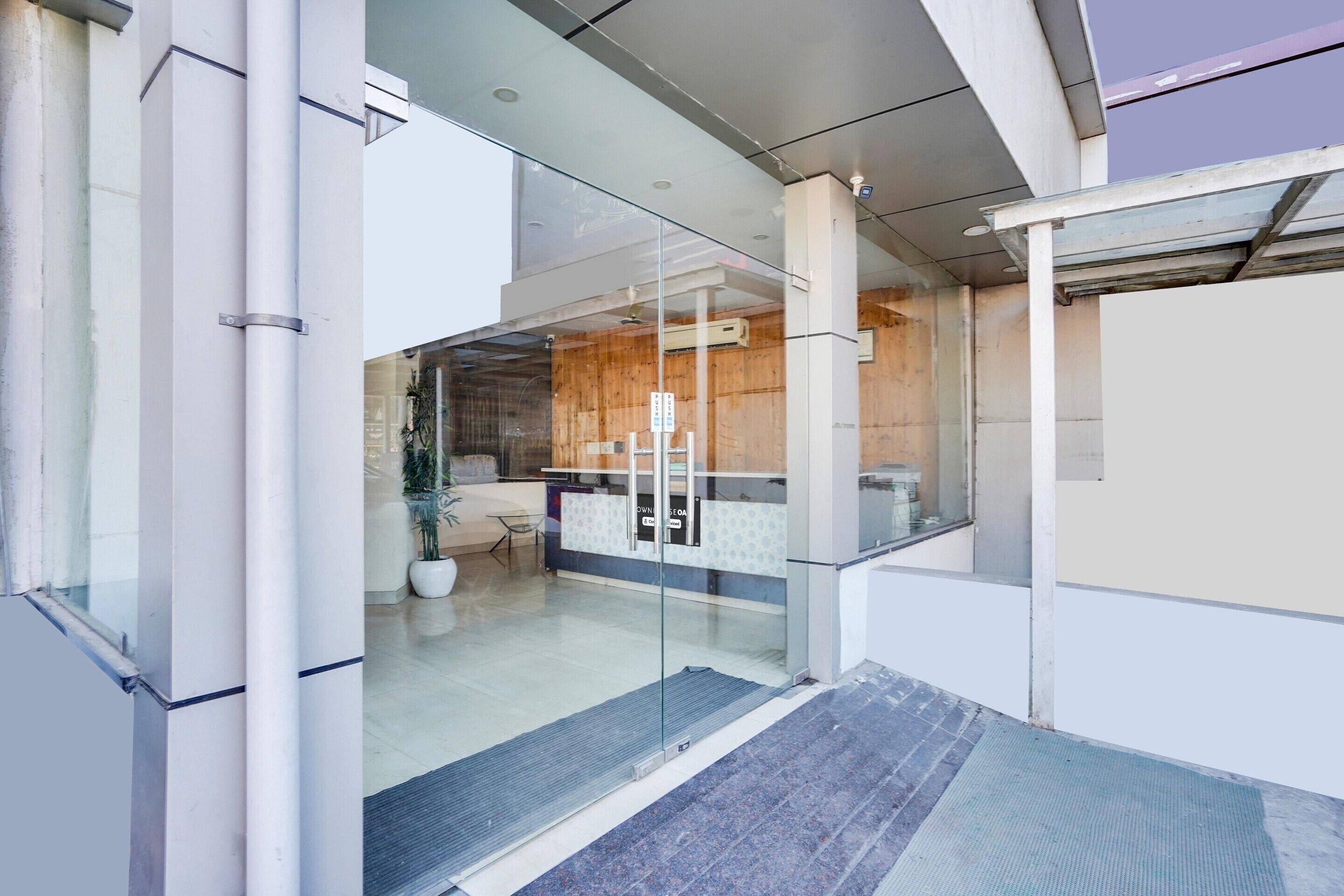 A modern hotel lobby with glass doors, a reception desk, and a seating area.