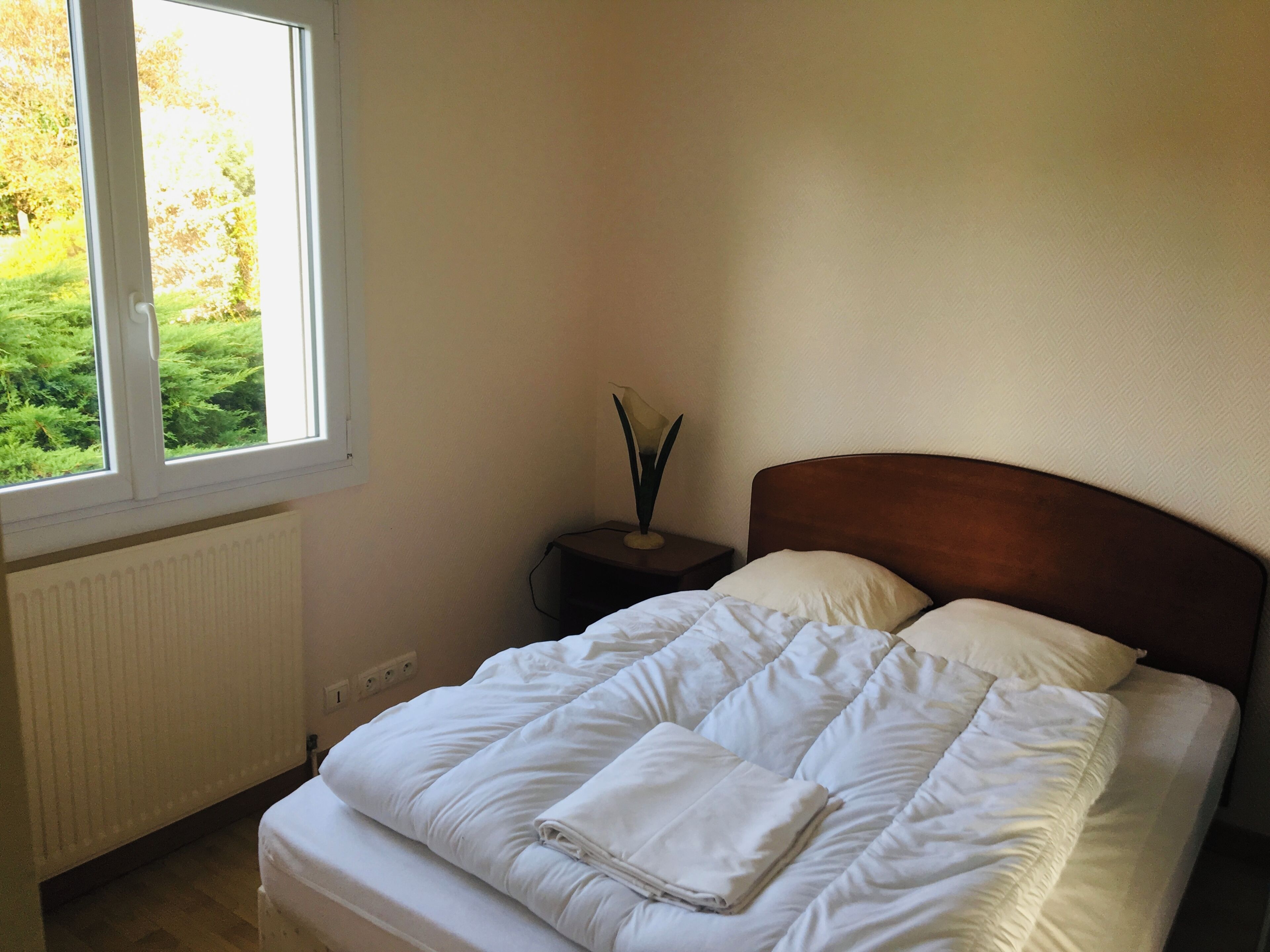 Ein Schlafzimmer mit einem Bett, einem Nachttisch, einem Fenster und einer Heizung.