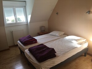 Ein Schlafzimmer mit zwei Betten, einem Fenster mit Jalousien, einem Nachttisch mit Lampe und einer Heizung.