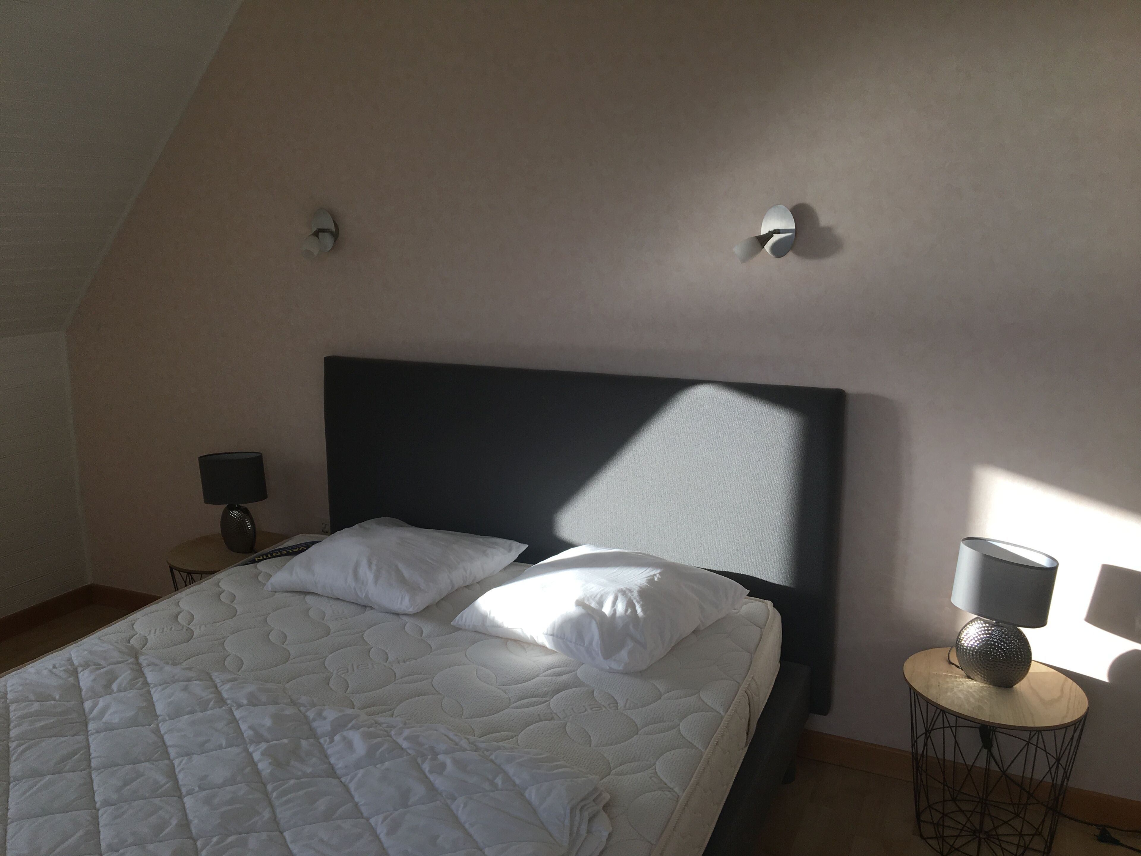 Een slaapkamer met een bed, een nachtkastje, een lamp en een wandlamp.